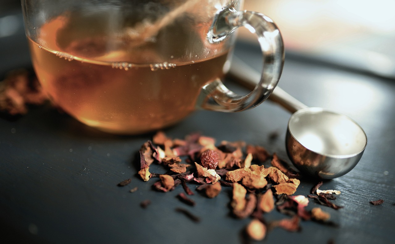 淹れたてのブレンドハーブティーが入ったガラスのカップとテーブルに散りばめられたドライハーブ